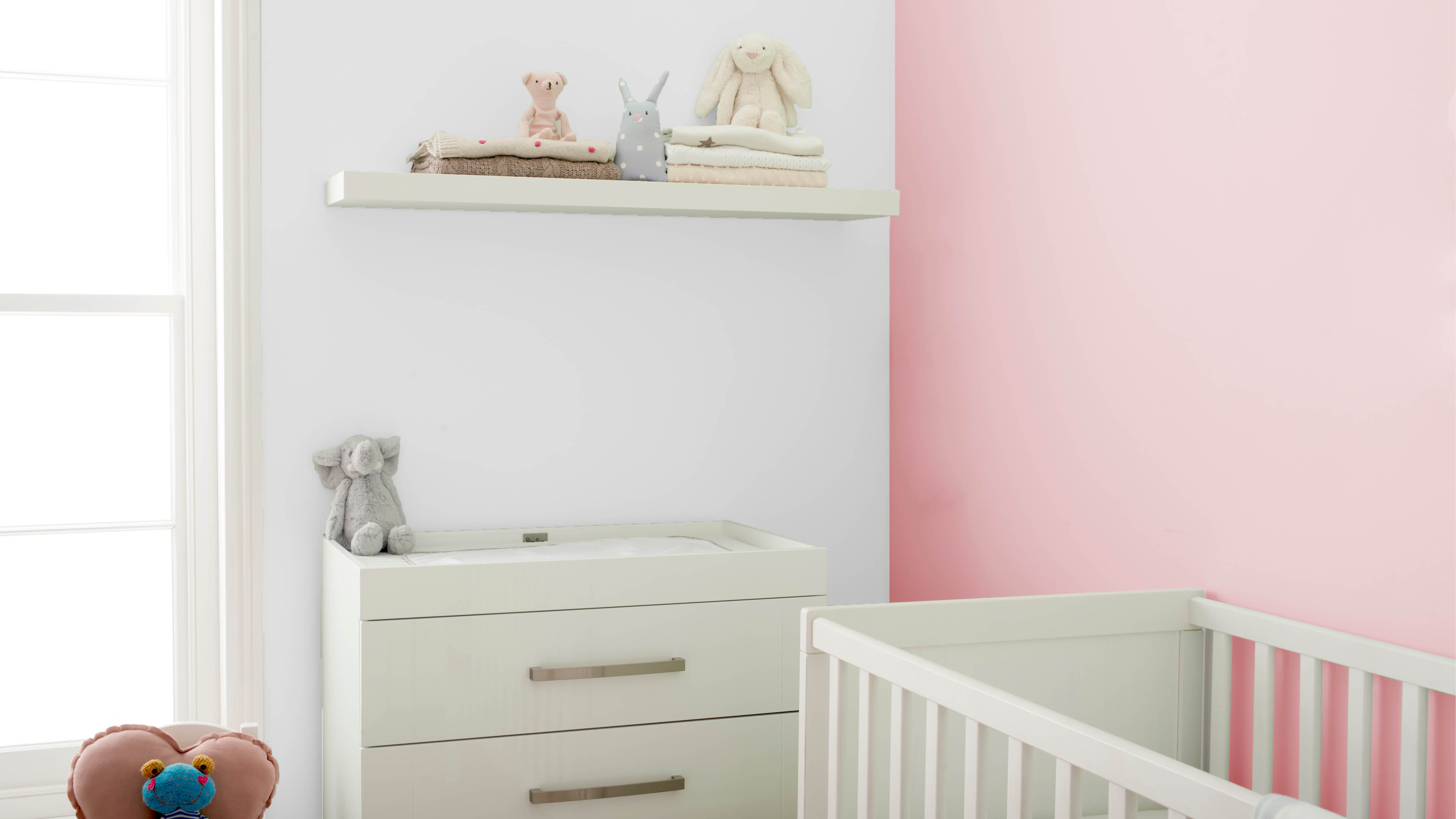 Une chambre de bébé rose avec des étagères à fixation invisible Une commode et des étagères à fixation invisible blanches sont la solution idéale pour ranger les couches et autres articles de puériculture.